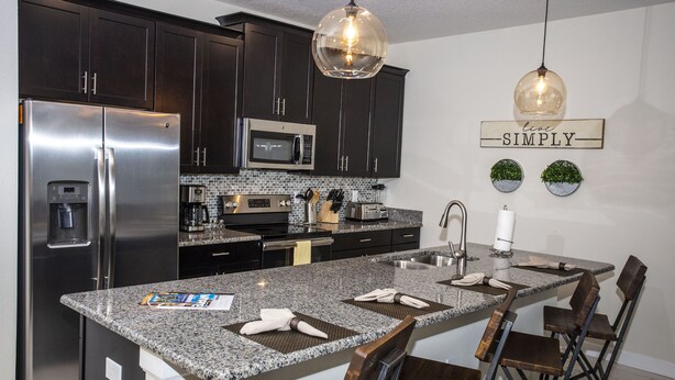 A modern kitchen with dark cabinets, stainless steel appliances, a granite countertop, and a central island with bar stools.