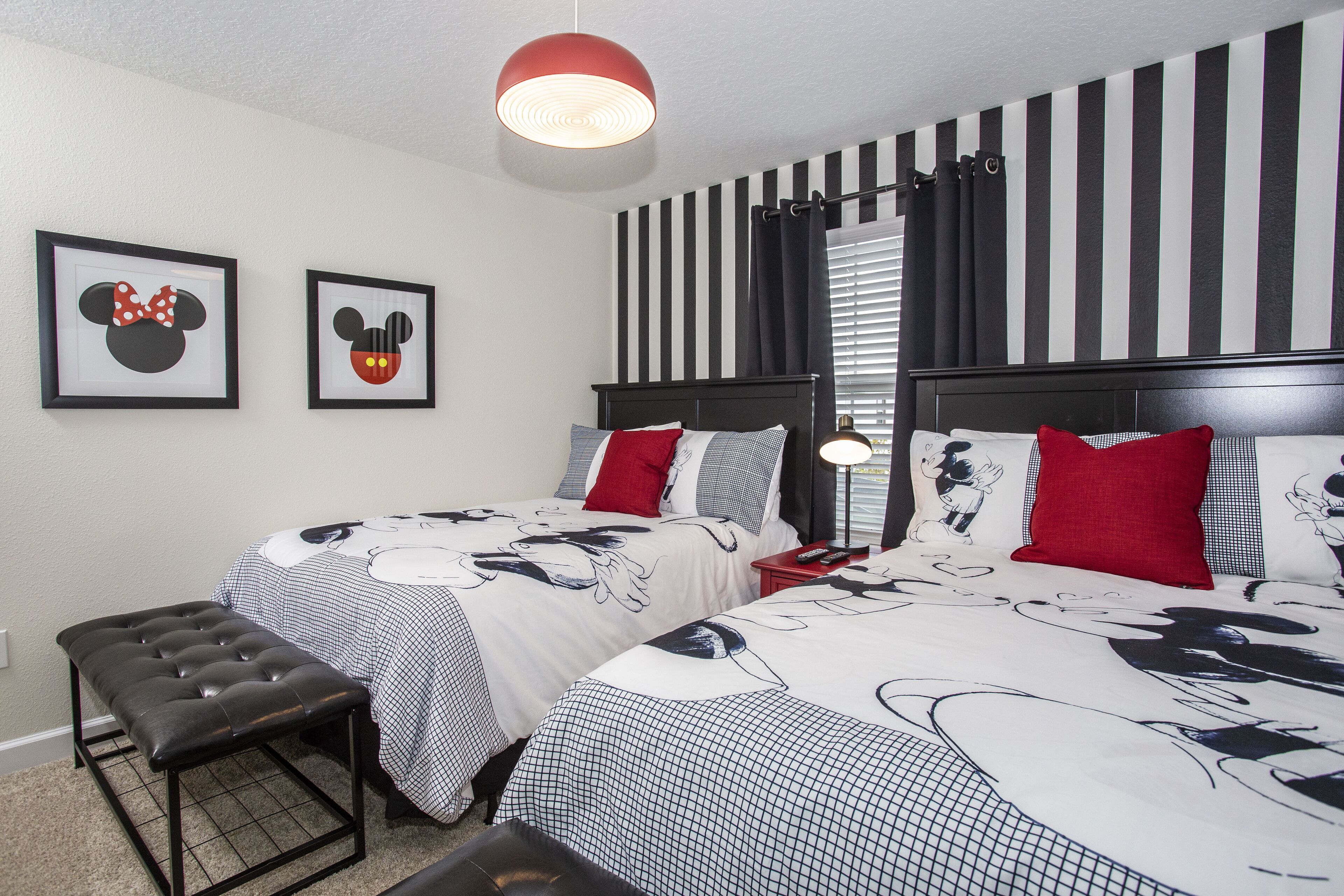 A hotel room with two beds, a bench, and Mickey Mouse themed decor.