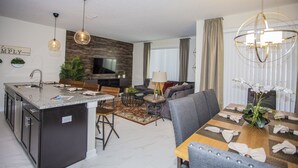 A modern kitchen with a central island, dining area with a table set for four, and a living room with a sofa and a TV.