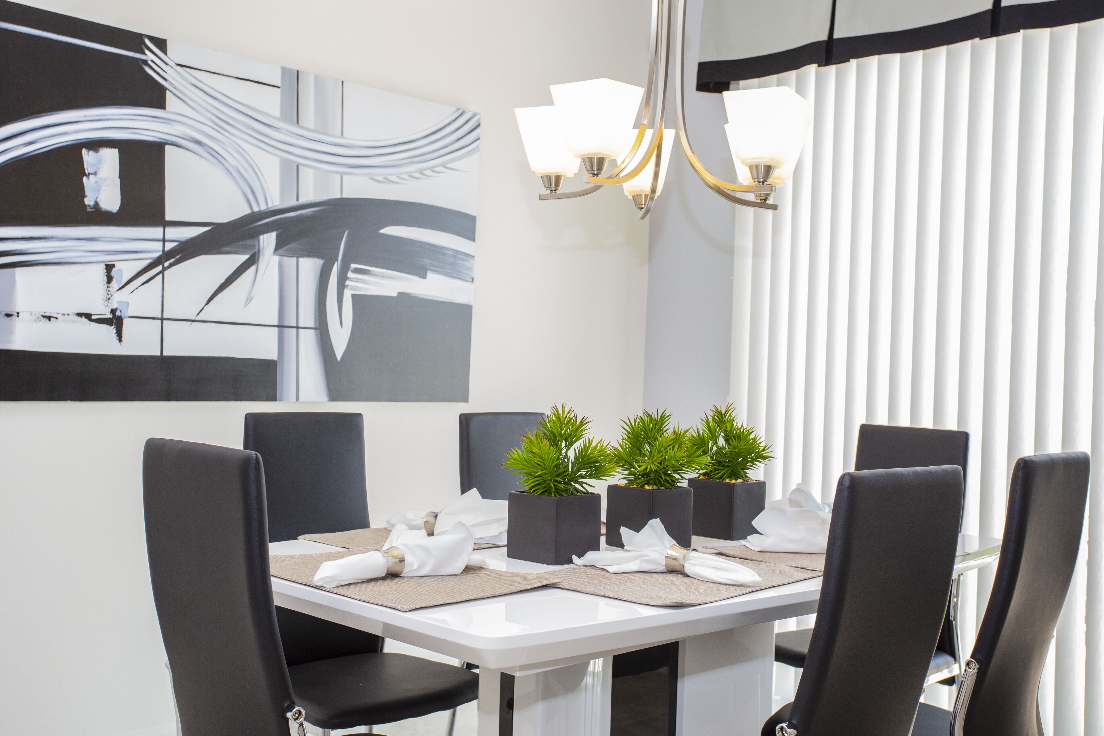 Un espace repas moderne avec une table blanche, des chaises noires et une peinture abstraite contemporaine accrochée au mur.