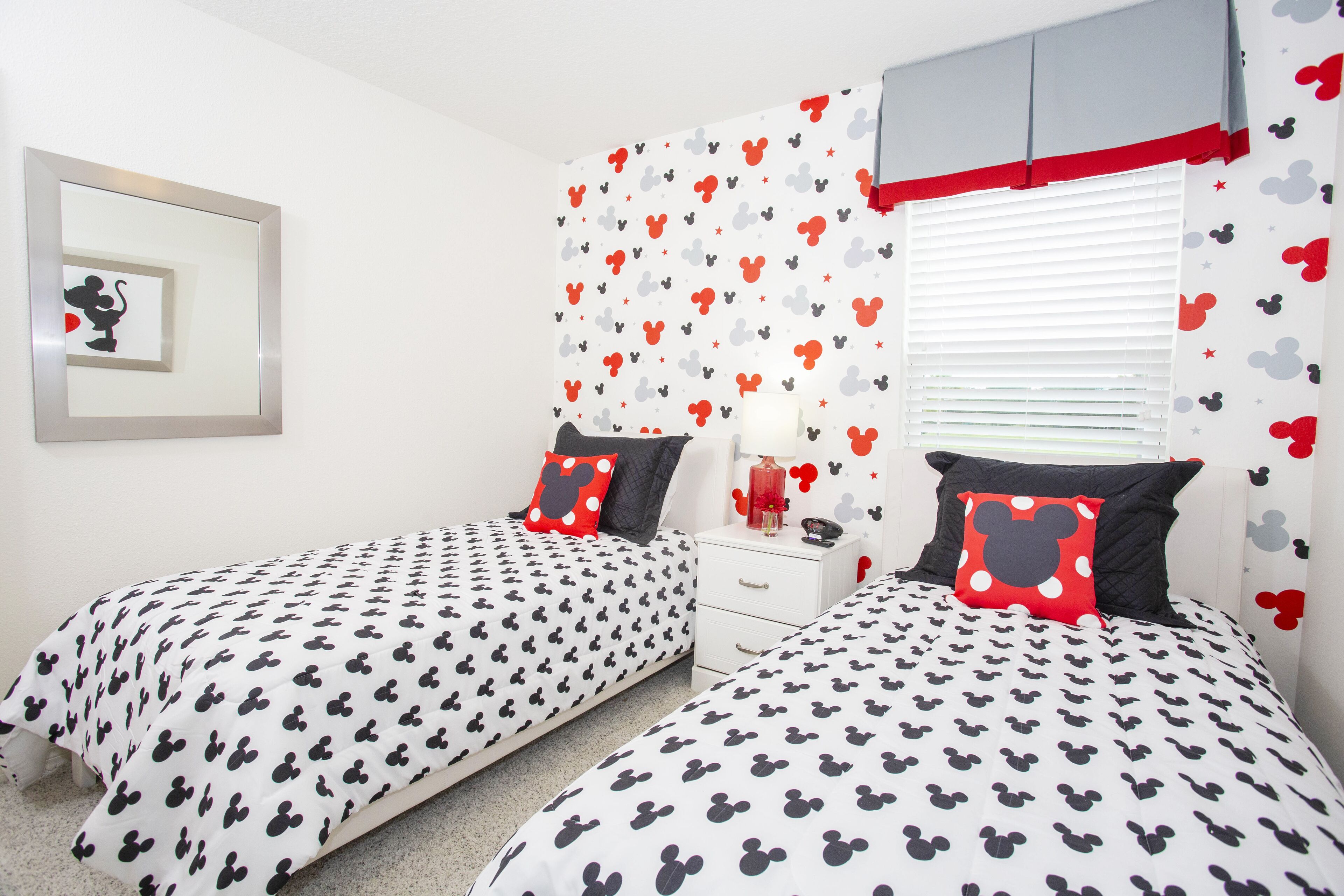 A bedroom with two beds, each with Mickey Mouse themed bedding, a bedside table with a lamp, and a framed picture on the wall.