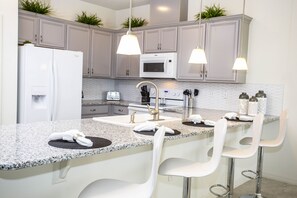 A modern kitchen with granite countertops, white bar stools, a built-in microwave, and pendant lighting. - Cozy Family Friendly 4Bd Close to Disney 5149 (Kissimmee)