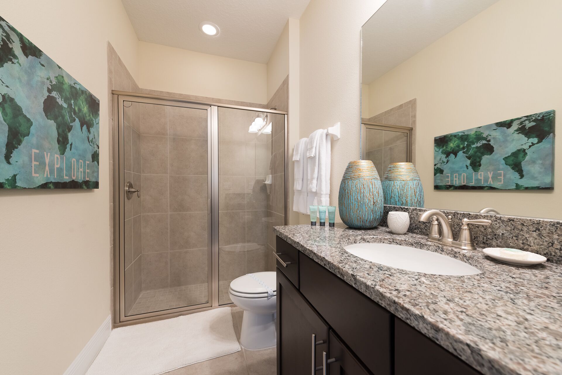 A modern bathroom with a glass shower enclosure, a white toilet, and a granite countertop with a sink and vanity.