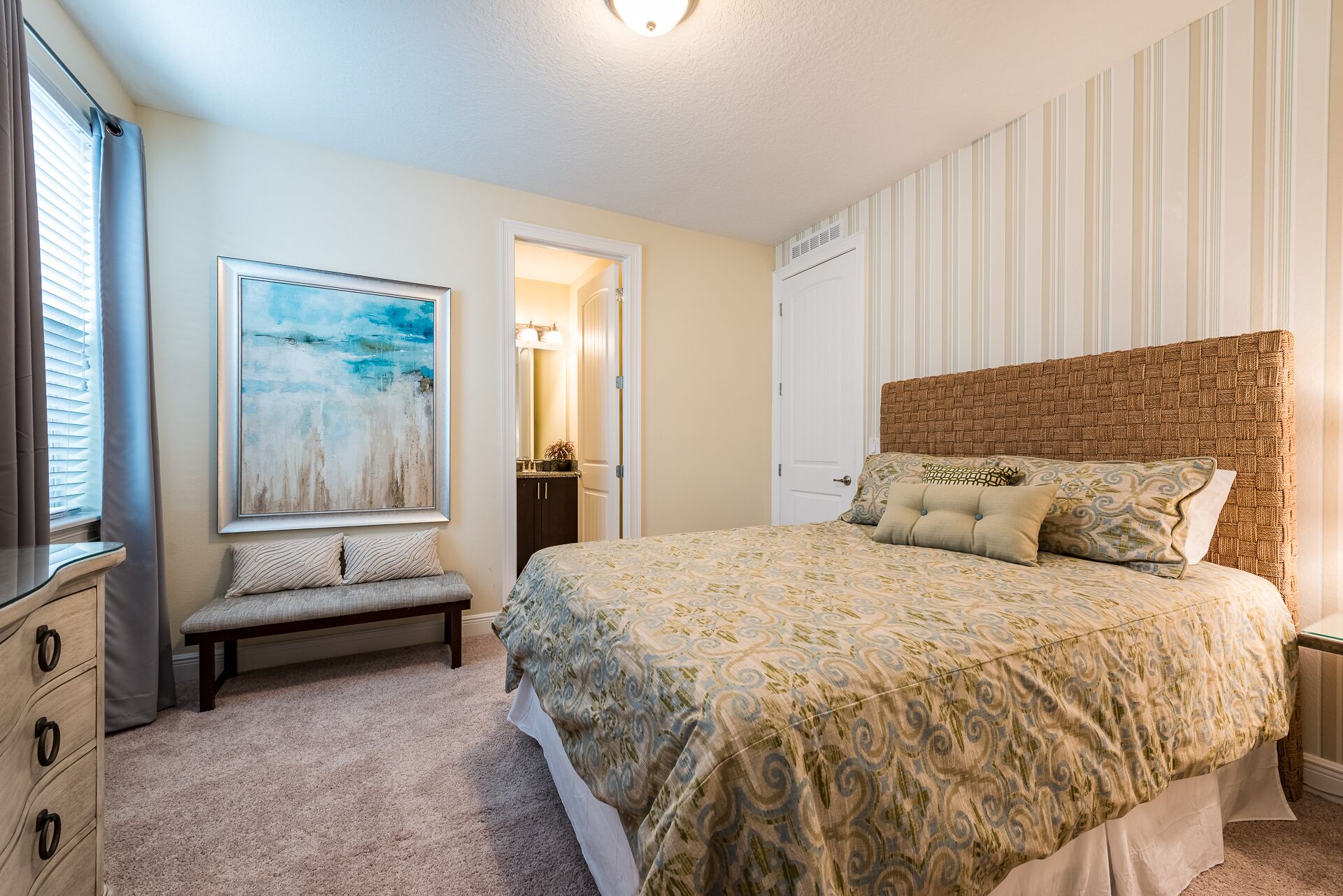 A bedroom with a large bed, a bench, a dresser, and a painting on the wall.