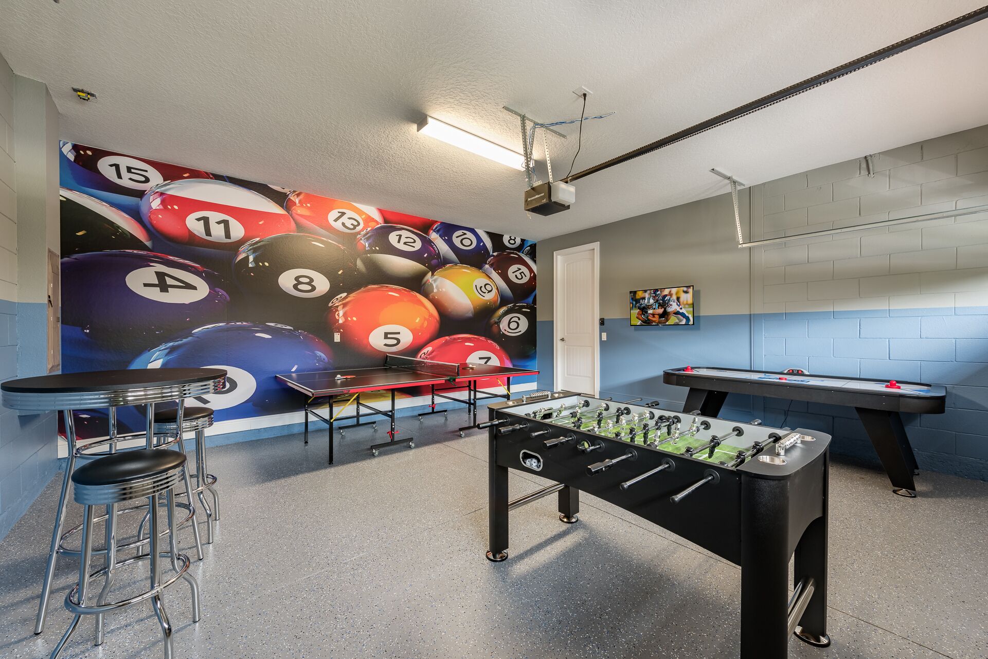 A billiards room with a pool table, foosball table, and a wall mural of billiard balls.