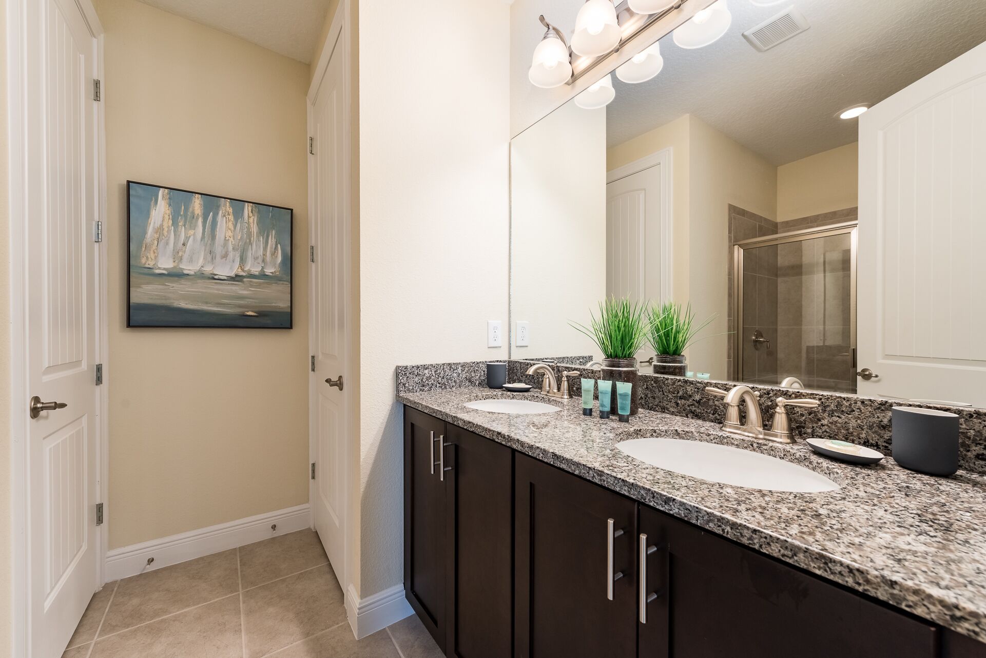 A bathroom with two sinks, dark cabinets, a painting of sailboats, and a large mirror.