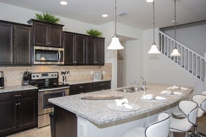 A modern kitchen with dark cabinets, stainless steel appliances, a granite countertop, and a white island with bar seating.