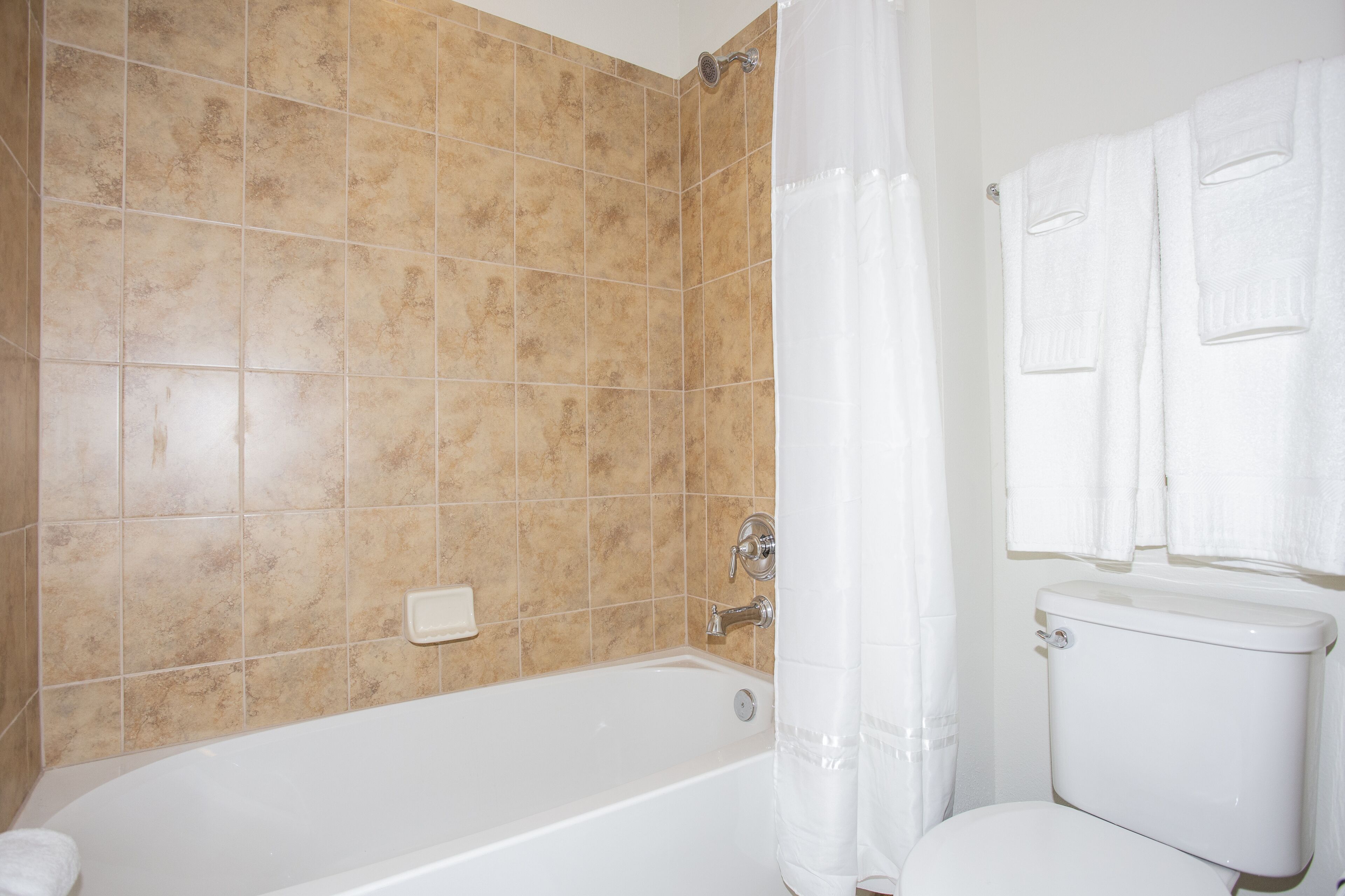 Ein Badezimmer mit beigen Fliesen, einer weißen Badewanne, einer weißen Toilette und einer Duschvorhang.