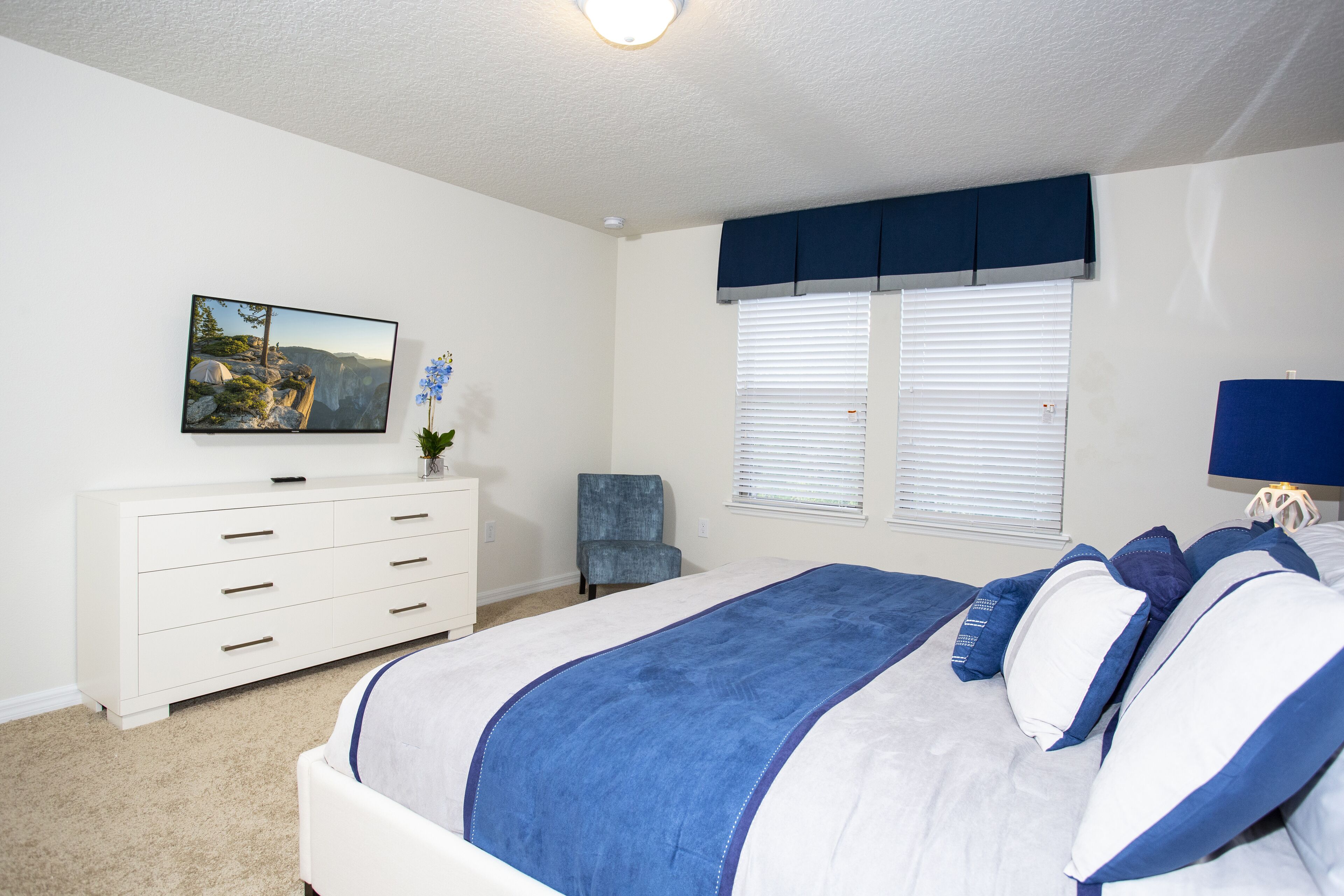 A bedroom with a bed, a dresser, a chair, a window with blinds, and a painting on the wall.