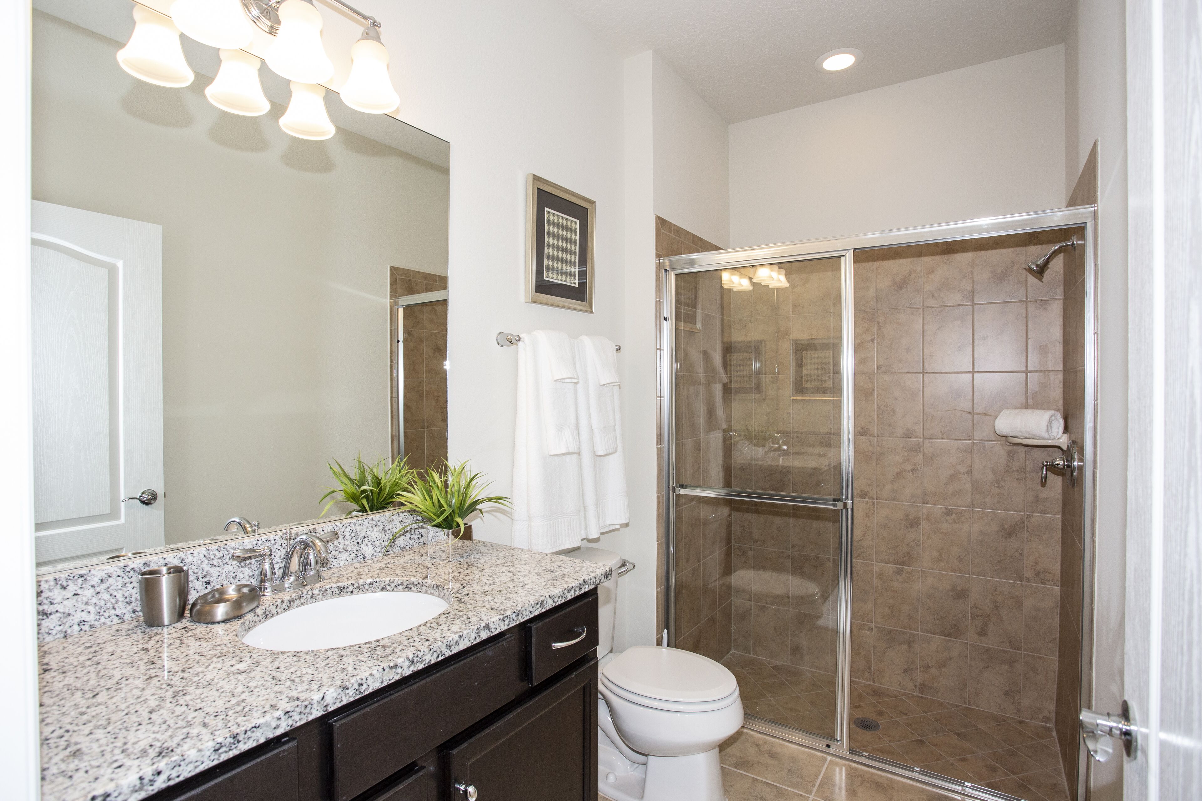 Un baño con encimera de granito, un lavabo blanco, un espejo, ducha con puerta de cristal y un inodoro.