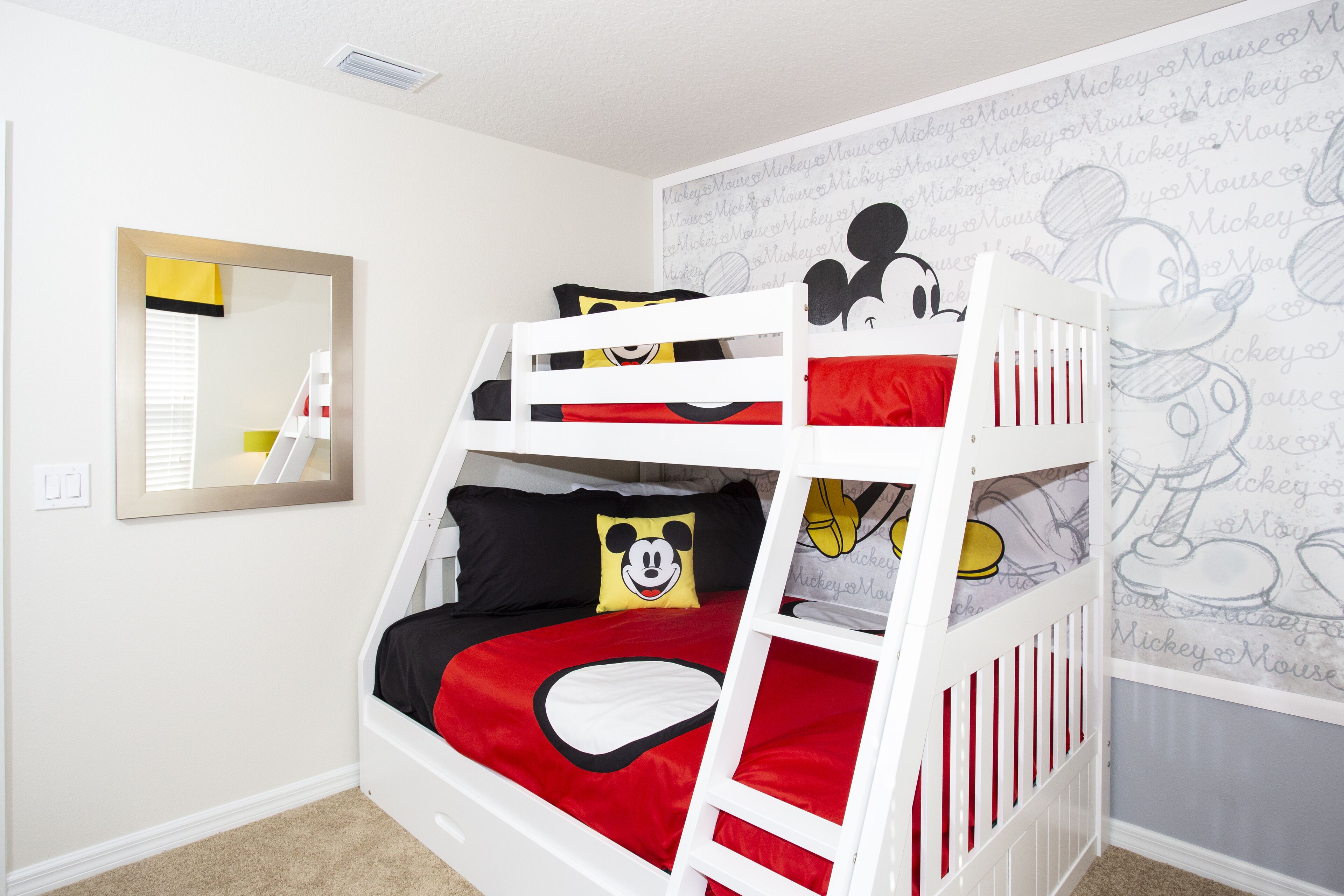 Una cama individual con ropa de cama temática de Mickey Mouse, un espejo y papel tapiz de Mickey Mouse.