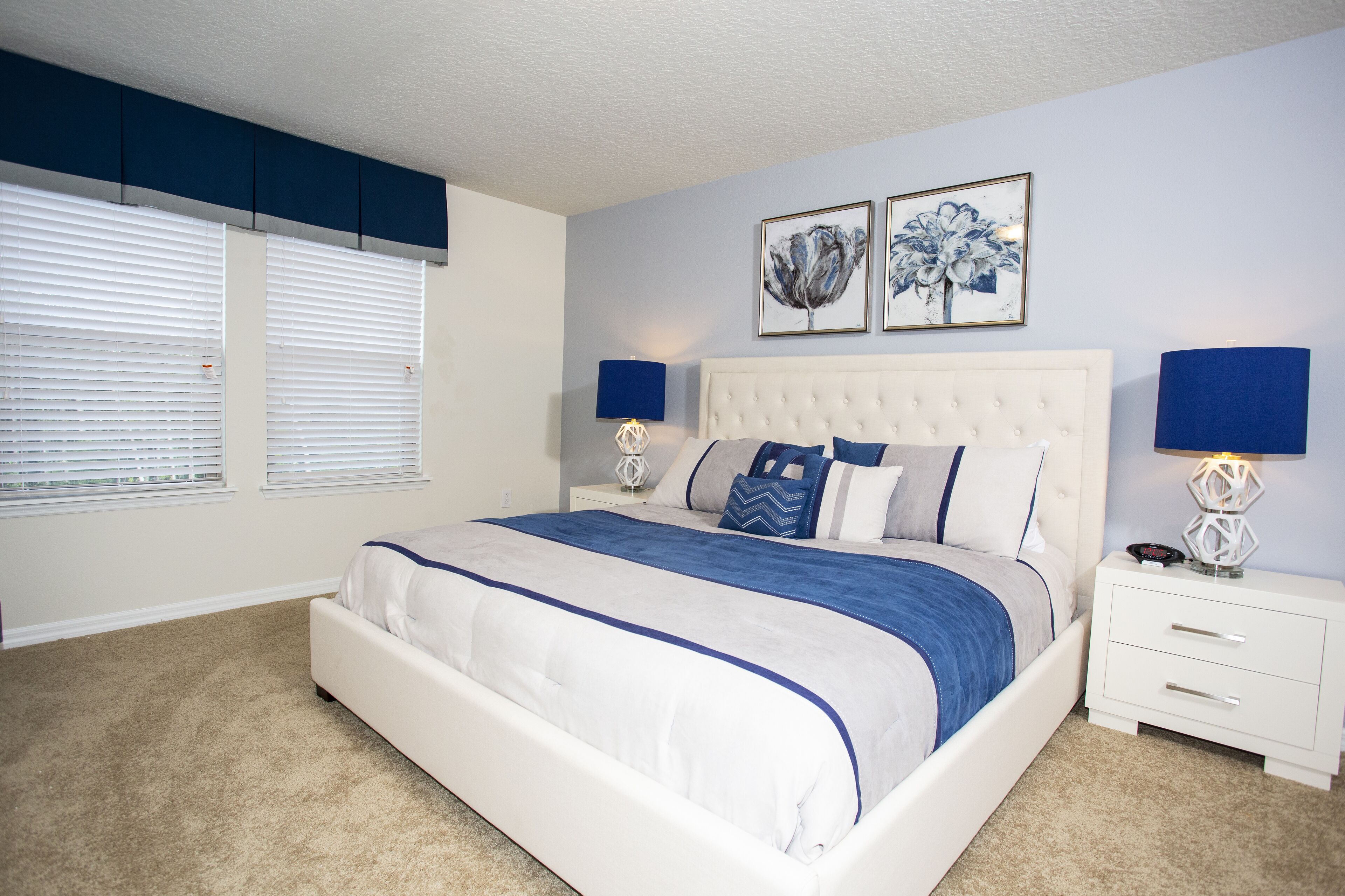A bedroom with a large bed, white nightstands, and wall-mounted lamps.