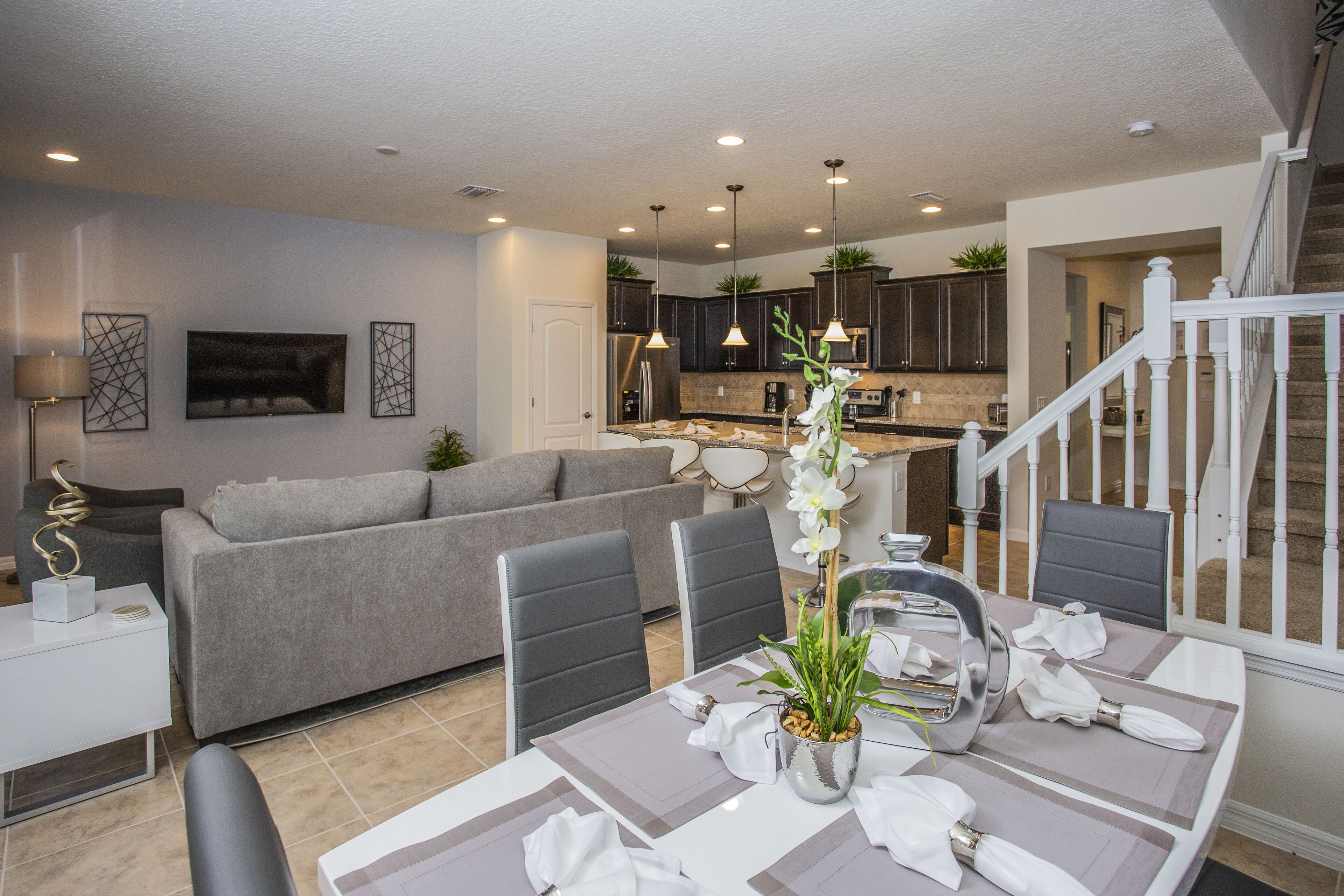 A modern living room with a grey sofa, dining table set with white tableware, and a staircase leading to another level.