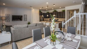 Un salon moderne avec un canapé gris, une table à manger dressée avec de la vaisselle blanche et un escalier menant à un autre niveau.