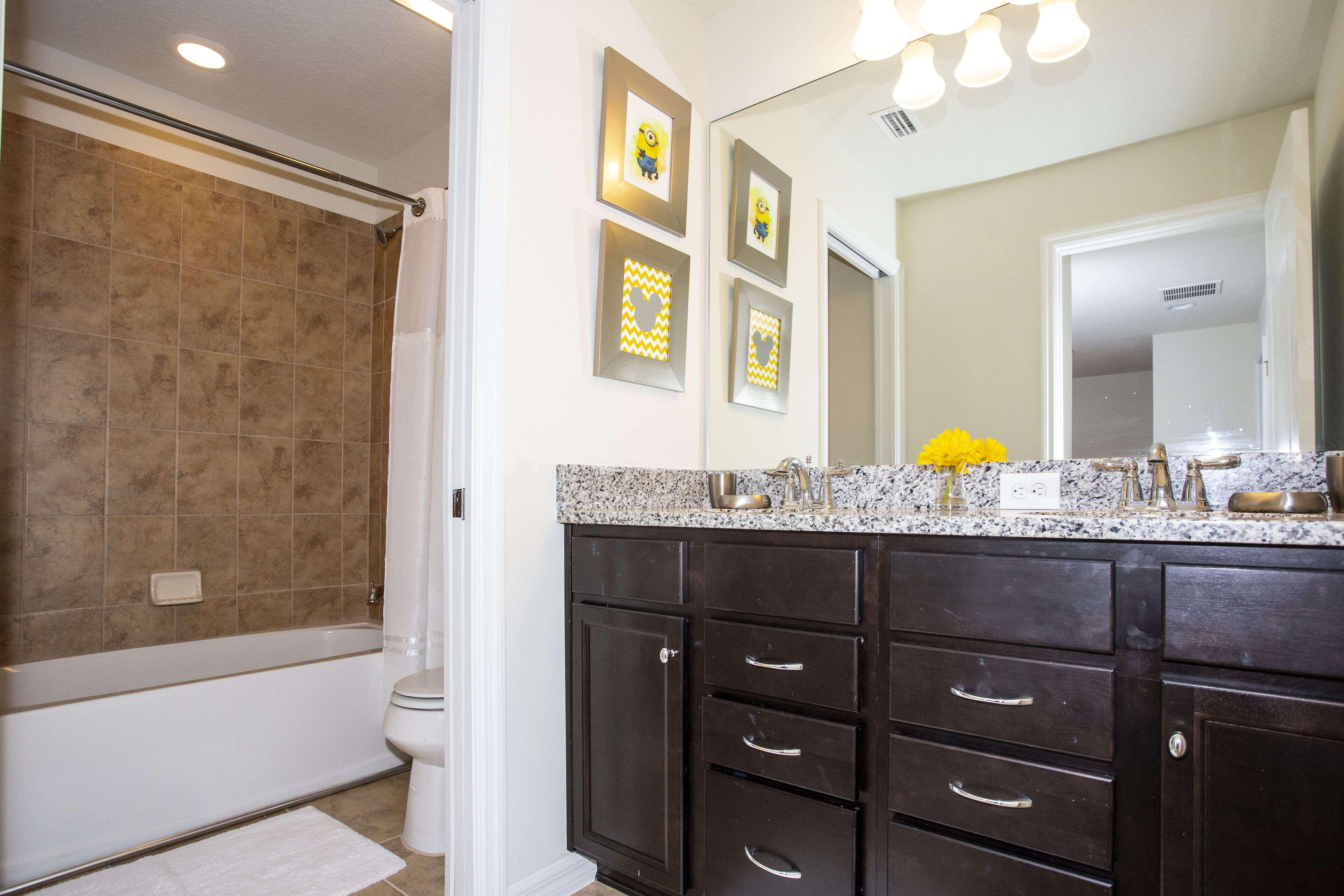 A bathroom with a bathtub, dark wooden cabinets, a granite countertop, and a mirror with three framed pictures.
