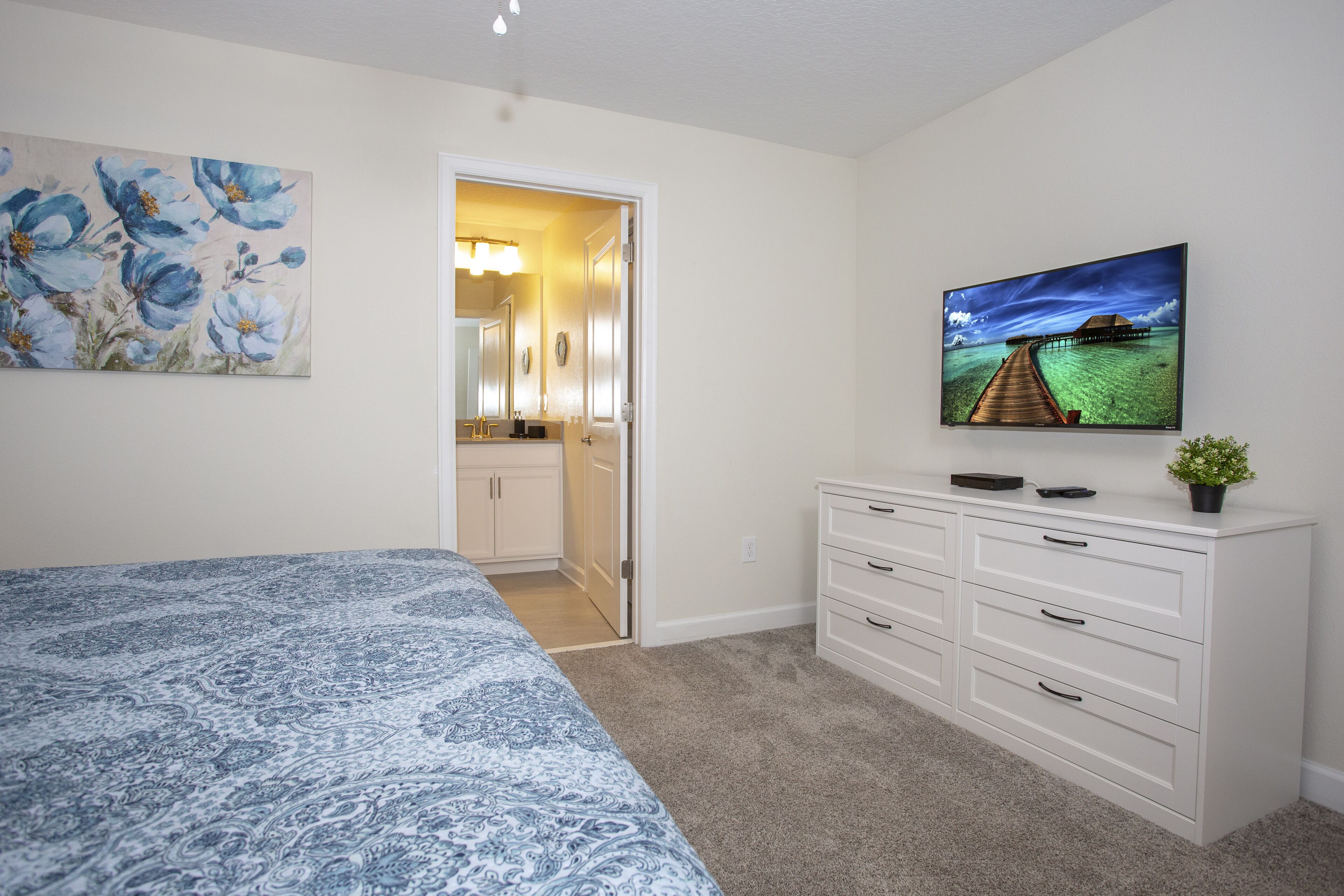 Quarto com cama, cômoda, pintura e porta para um banheiro.