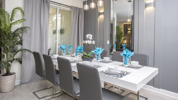 A modern dining area with a white table set for six, grey chairs, and a large mirror on the wall.