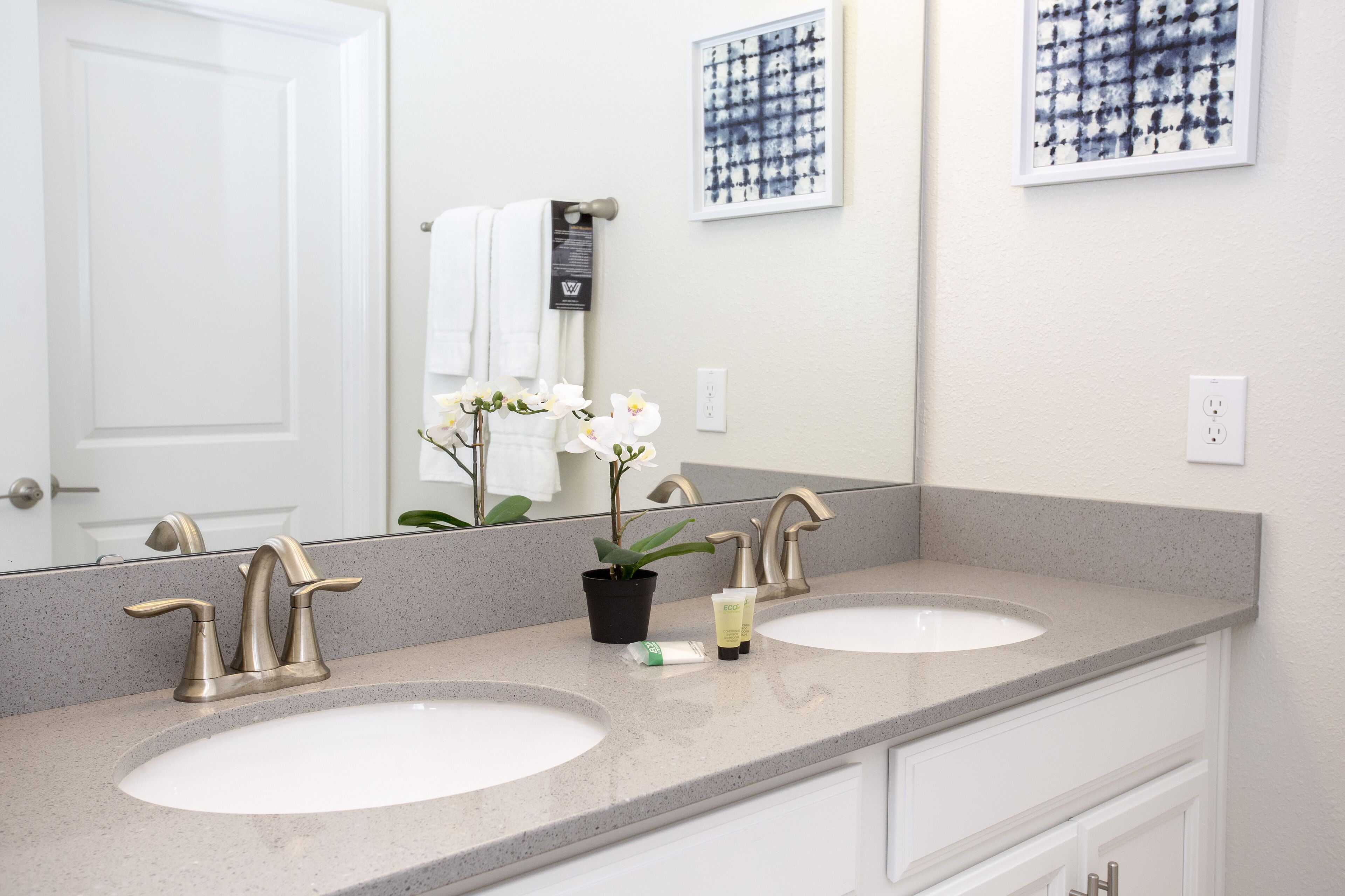 A bathroom with two sinks, a large mirror, and a potted orchid.