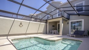 A swimming pool with a glass ceiling, a small table, and chairs, and a lounge chair.