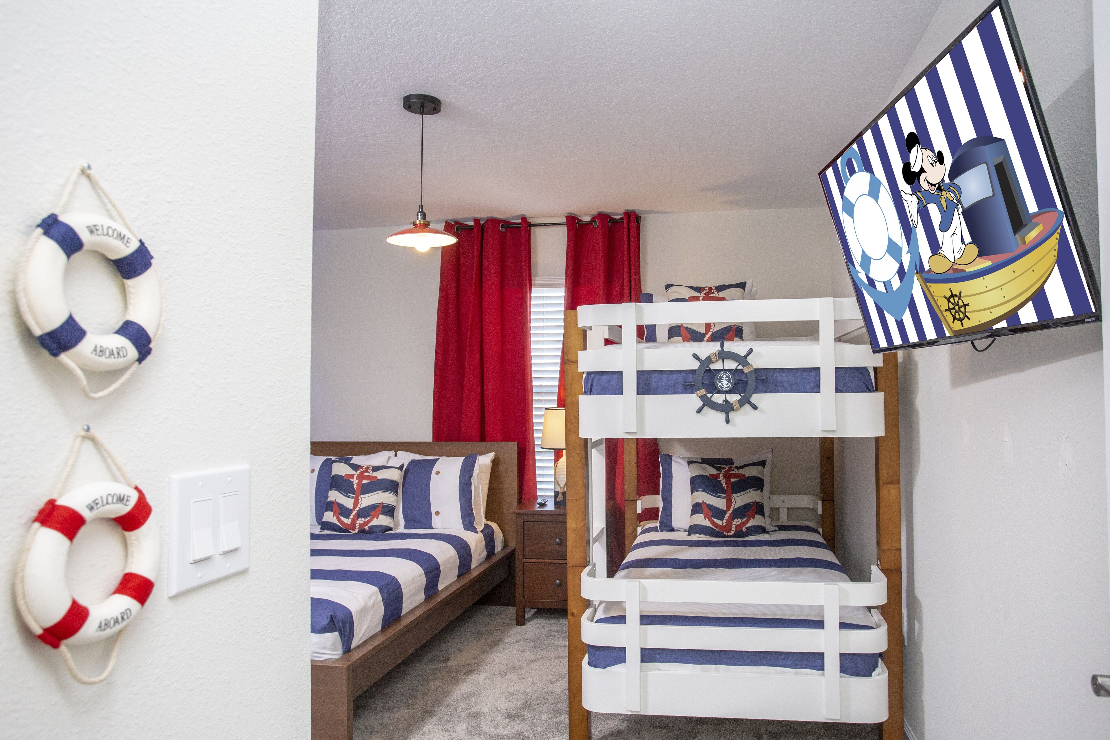 A room with bunk beds, nautical-themed bedding, life rings on the wall, and a TV displaying a cartoon character.