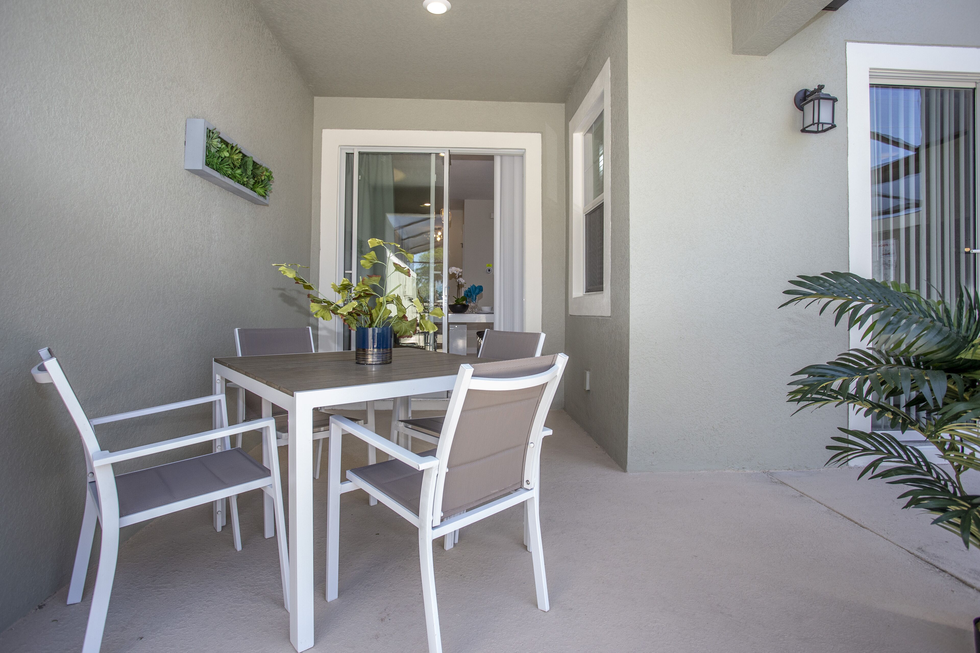 Un patio con una mesa y sillas, una planta en maceta y un ventanal corredero que da a un espacio interior.