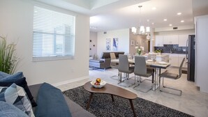 Una cocina moderna con armarios blancos, una zona de comedor con mesa y sillas, y una sala de estar con sofá y mesita de centro.