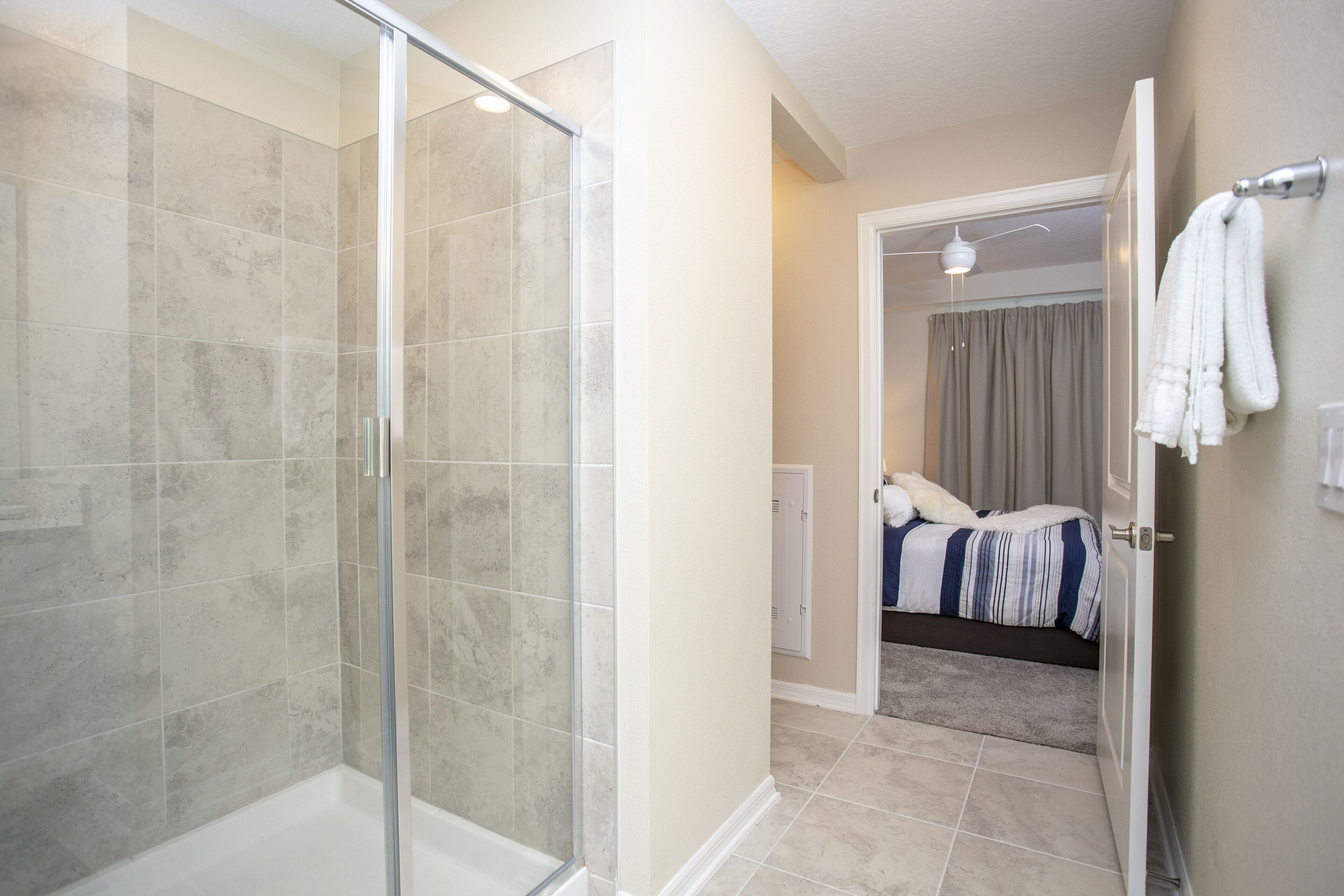 A modern bathroom with a glass shower enclosure and a separate bedroom with a bed and a bathroom.