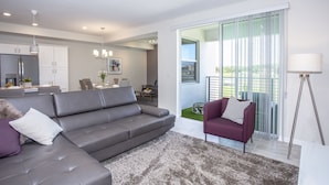 Una sala de estar moderna con un sofá gris, un sillón púrpura y un amplio ventanal con vistas a zonas verdes.