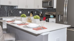 Una cocina moderna con armarios blancos, un refrigerador de acero inoxidable, un microondas y un horno empotrado.