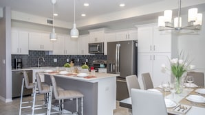 Una cocina moderna con armarios blancos, electrodomésticos de acero inoxidable y una isla central con taburetes de bar.