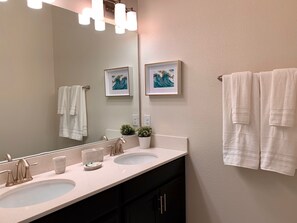 Une salle de bain avec deux lavabos, un grand miroir et des serviettes accrochées au mur.