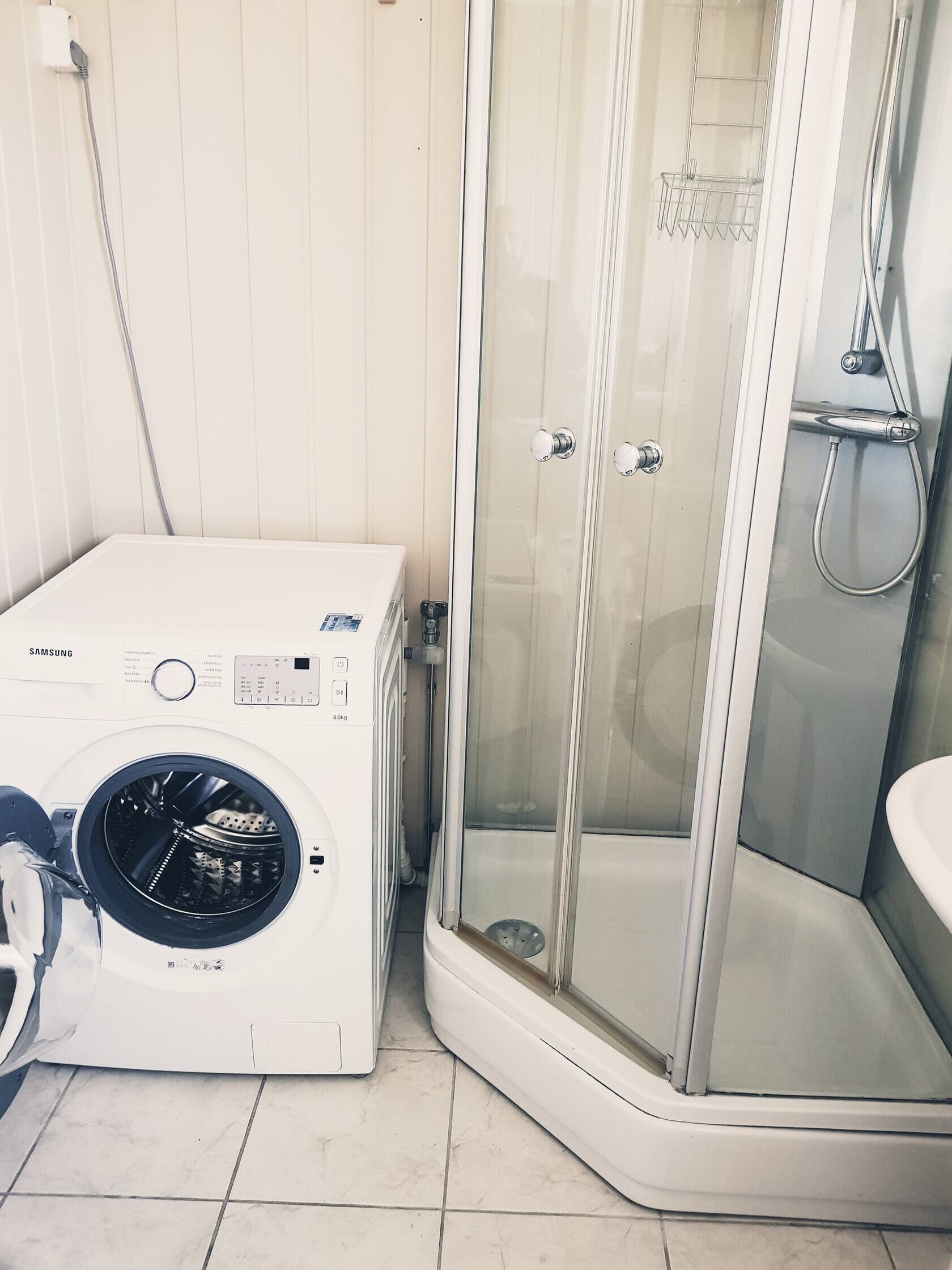 Un bagno compatto con lavatrice, box doccia in vetro e lavandino.
