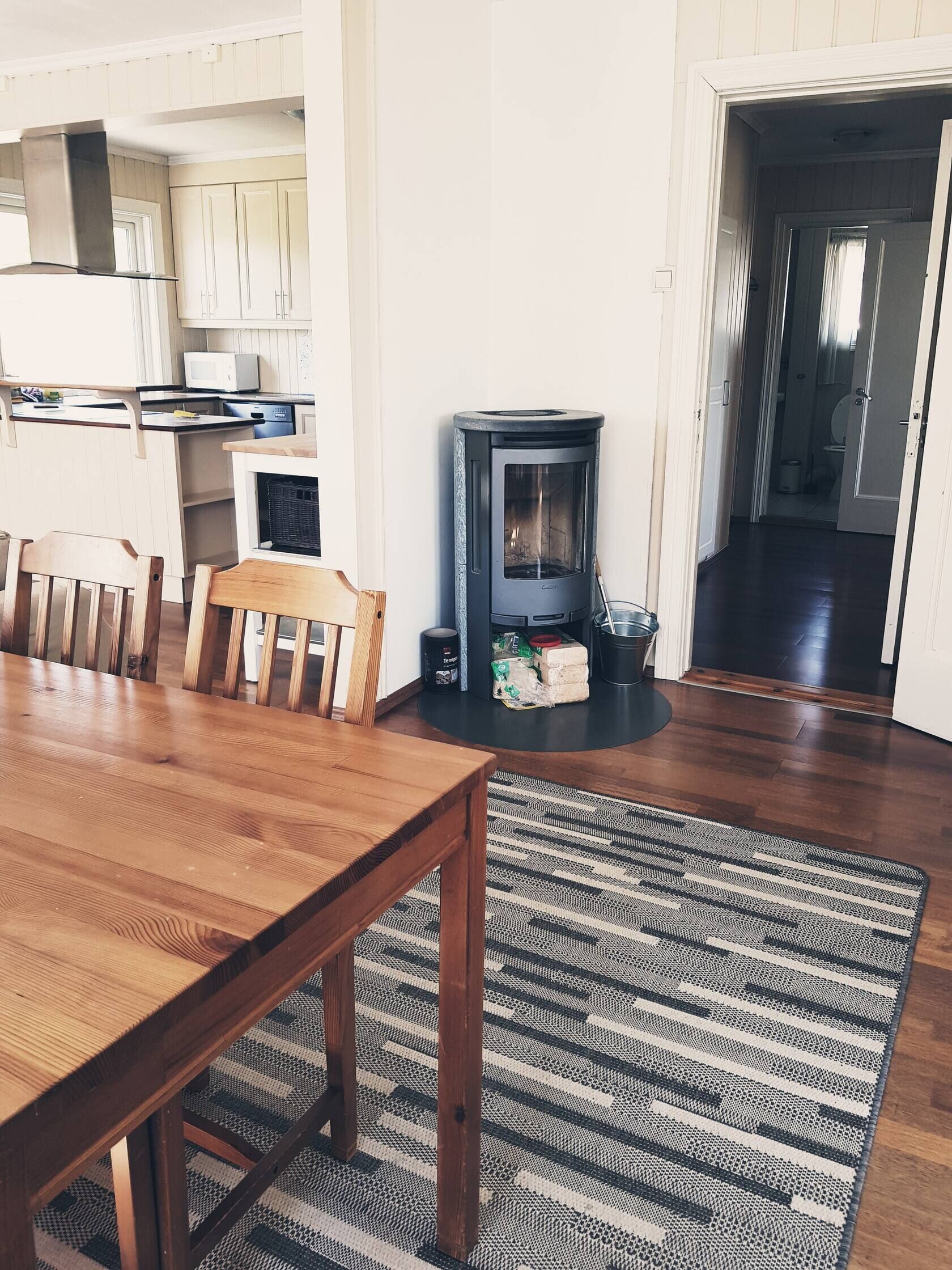 Un comedor con una mesa y sillas de madera, una estufa negra, y una cocina al fondo.