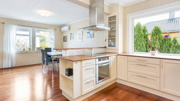 A modern kitchen with a central island, built-in oven, and a large window offering a view of greenery.