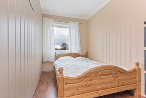 A small, single-bed room with wooden headboard, white curtains, and a window with a view of trees. - StayPlus 3BR City Apartment With Garden (Kristiansand)
