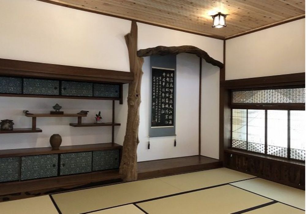Habitació japonesa tradicional amb sòls de tatami, una estant de fusta amb objectes decoratius, un pergamí penjat i una finestra amb un disseny d'entramat.