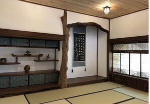 Una habitación japonesa tradicional con suelo de tatami, un estante de madera con adornos, un pergamino colgado y una ventana con diseño de celosía.