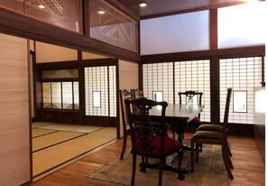 Una habitación japonesa tradicional con suelo de tatami, una mesa baja, sillas de madera y puertas correderas con diseños de cuadrícula.