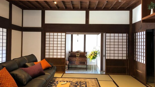 A traditional Japanese-style room with tatami flooring, a black leather sofa with orange cushions, a wooden cabinet, and a ceiling fan. - A 100-year-old folk house has been completely renewed, and you can enjoy living in a satoyama in just one hour from the Tokyo metropolitan area via the Aqua- Line / Ken-O Expressway. (長南町)