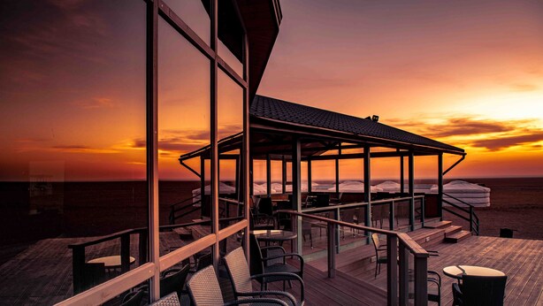 A deck with outdoor seating and a covered area, overlooking a beach at sunset. - Dream Gobi Lodge (Dalanzadgad)
