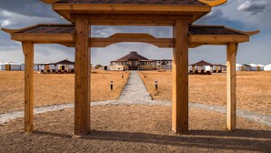 A wooden structure with a tiled roof, leading to a building with a red roof and multiple windows. - Dream Gobi Lodge (Dalanzadgad)