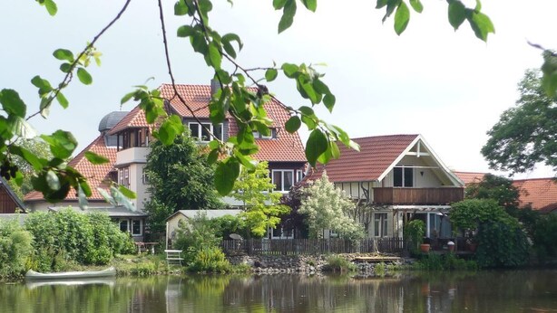 A house with a red-tiled roof, a pond in front, and a wooden fence. - Lake house with lake view 1  (Ilsenburg (Harz))