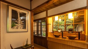 Un intérieur de style japonais traditionnel, avec un comptoir en bois, un tableau représentant une cascade encadré et une vue sur la verdure à travers de grandes fenêtres.