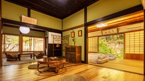 Une pièce de style japonais traditionnel, avec un sol recouvert de tatamis, une table basse, un canapé et une porte coulissante donnant sur un jardin.
