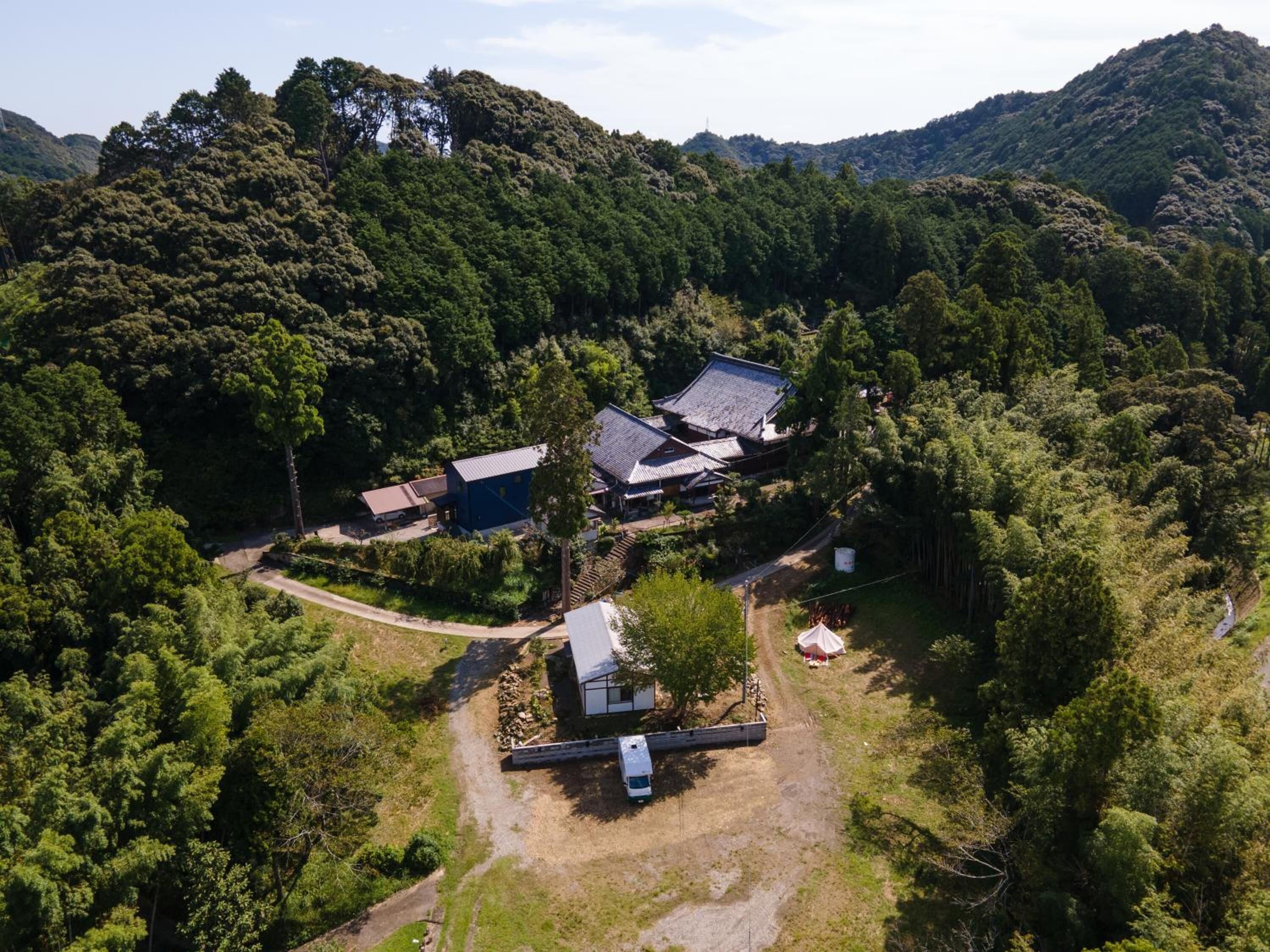 An aerial view of a rural property with traditional buildings, surrounded by dense forest and hills.