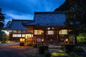 A traditional Japanese building with a tiled roof and wooden structure, surrounded by a gravel path and greenery.