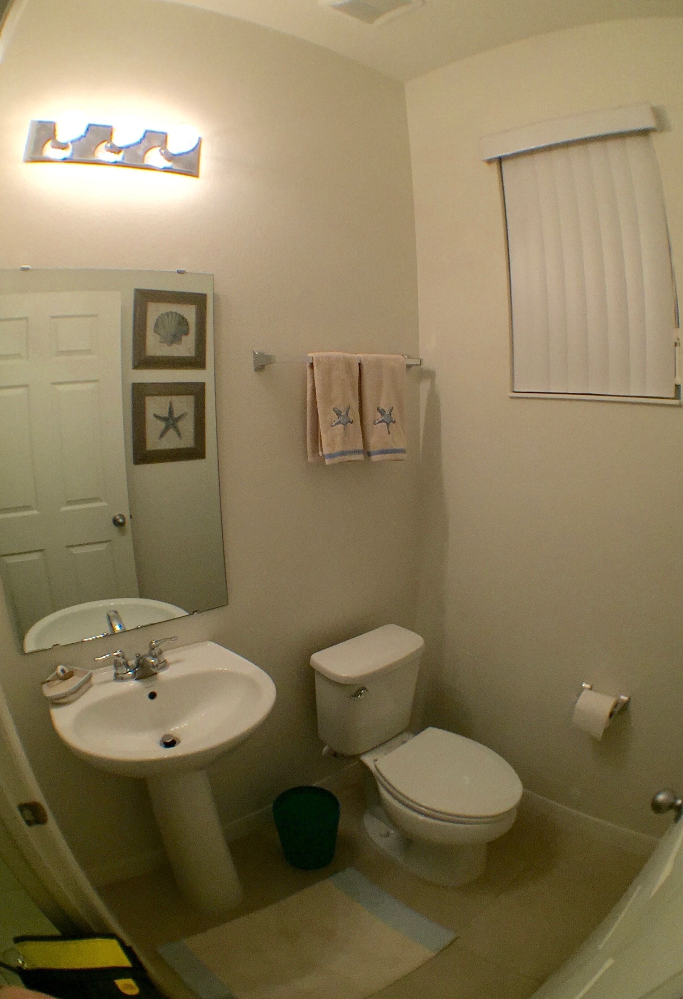 A compact bathroom with a sink, toilet, and a small window with blinds.