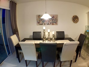 Une salle à manger avec une table noire, des chaises blanches et grises, et un lustre.