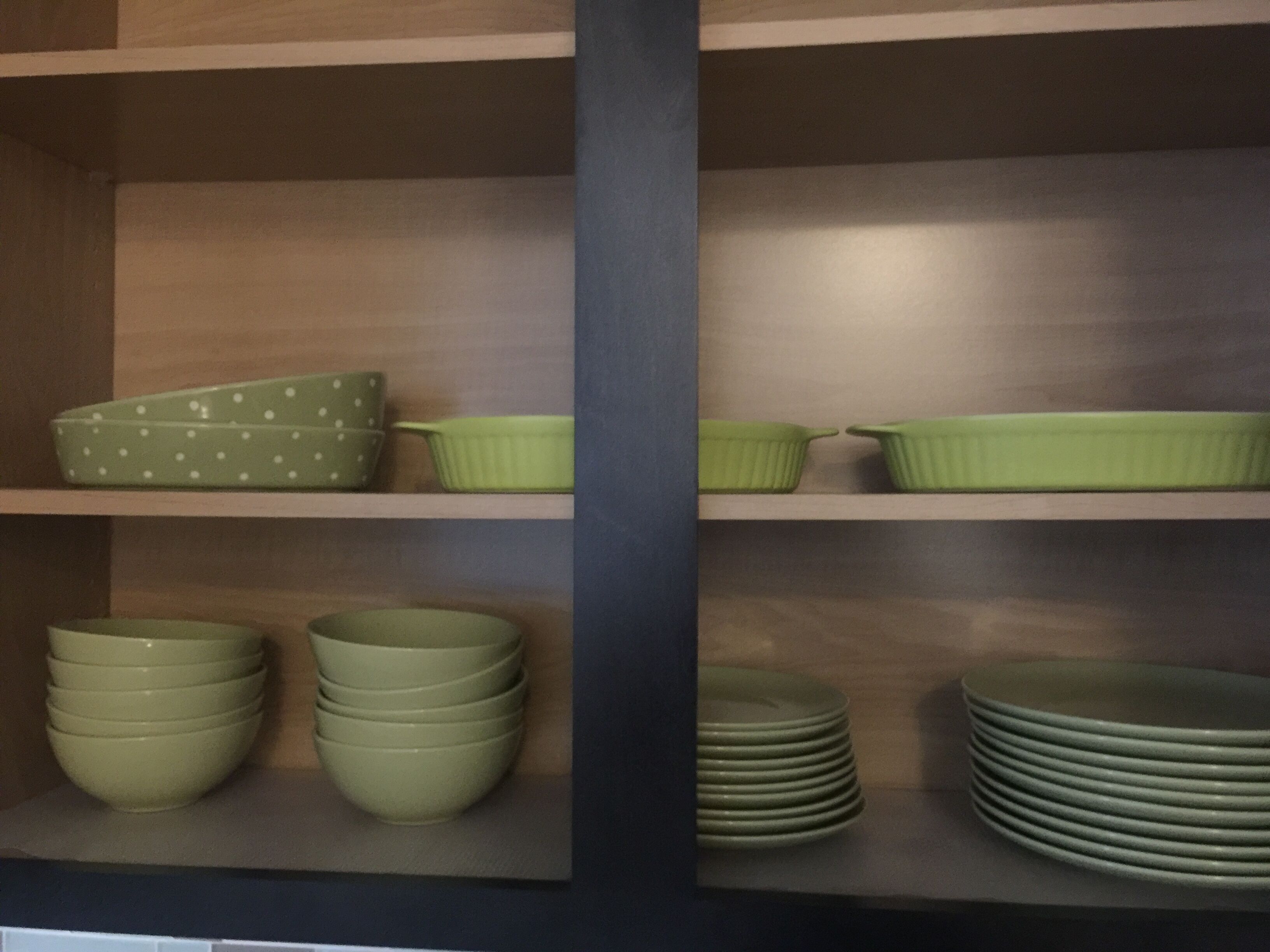 A kitchen with wooden shelves holding green bowls, plates, and a polka-dotted bowl.
