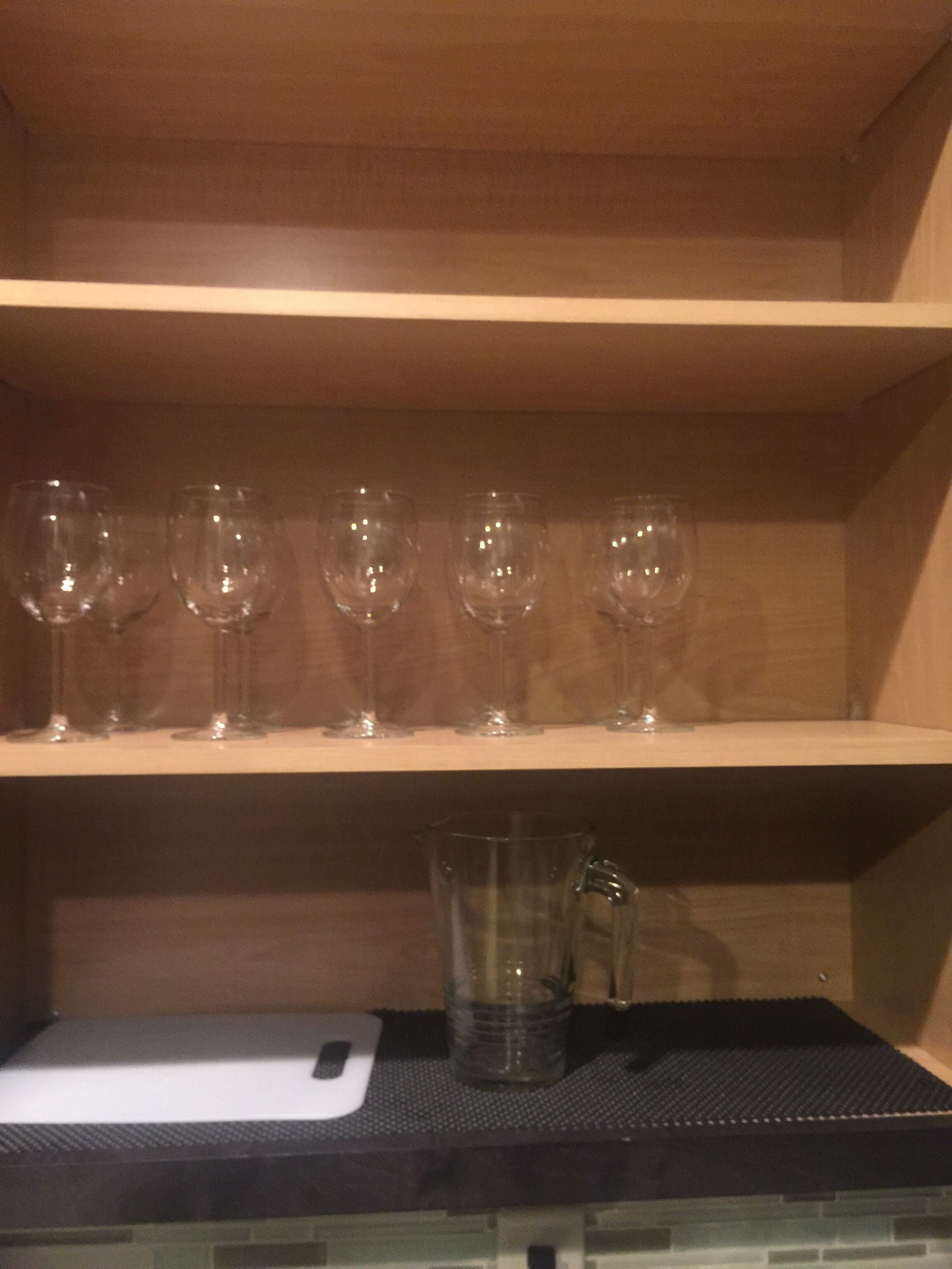 Une étagère avec six verres à vin et un pichet en verre, le tout posé sur un tapis noir.